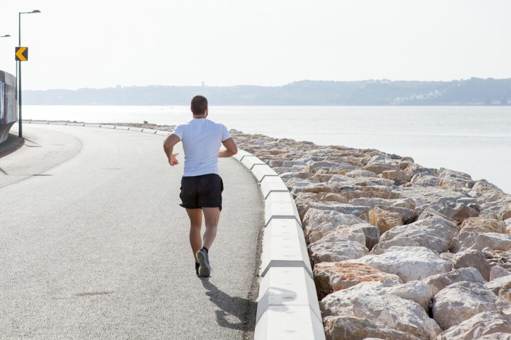 Back View of Strong Man Running on Seaside Road